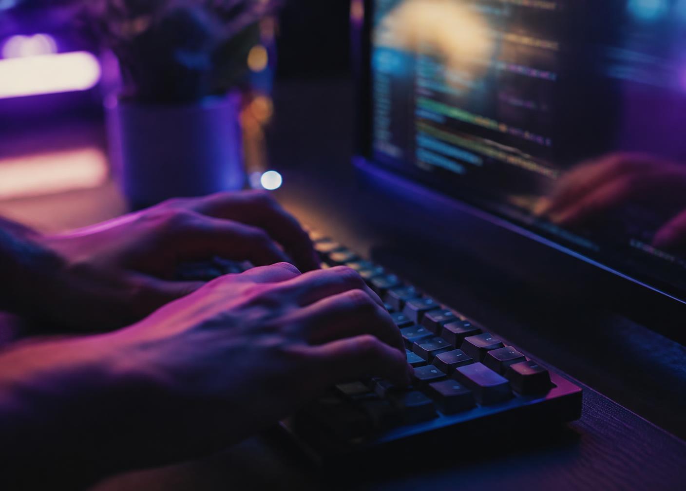Hands typing code on a keyboard in a dimly lit room